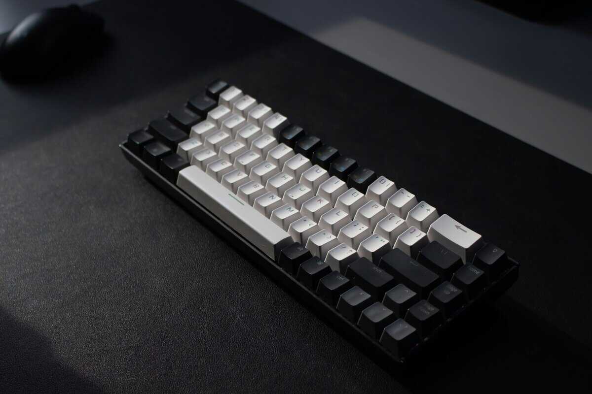 A 60% keyboard with black and white keycaps on a dark desk with a gaming mouse in the background.