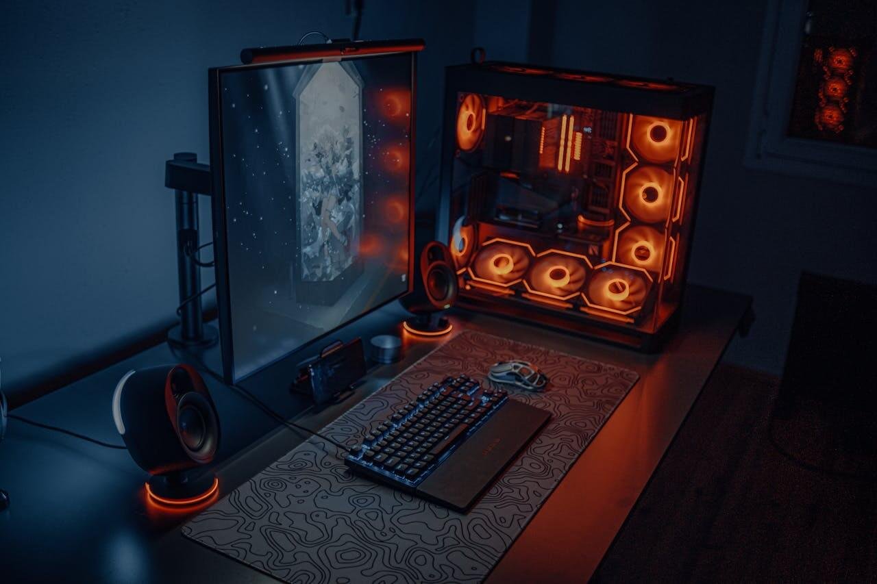 Sleek gaming desk setup featuring RGB lighting, large monitor, and gaming PC with glowing fans.