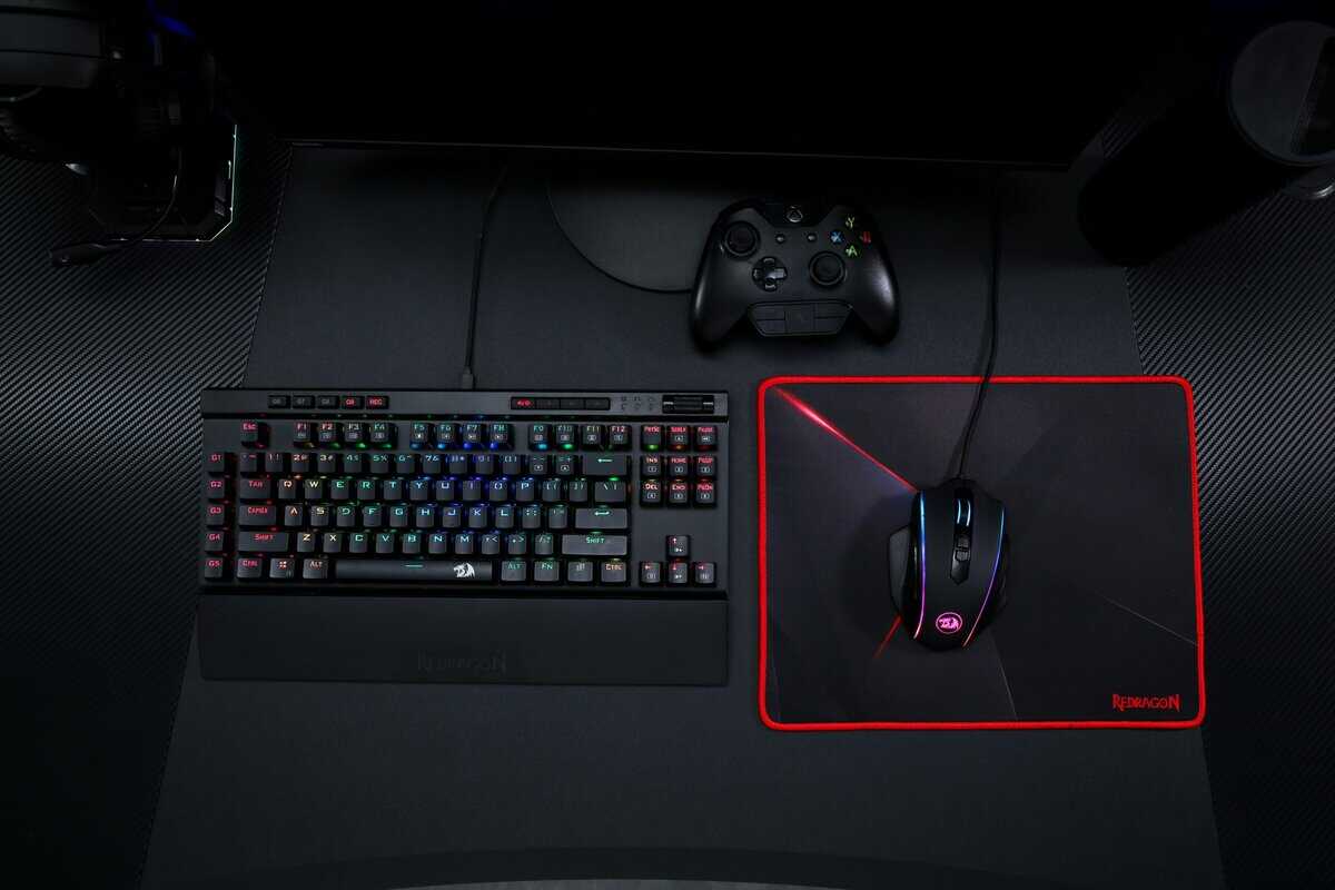 A gaming desk setup featuring the best budget gaming mouse pad from Redragon with red edges, RGB keyboard, and Xbox controller.