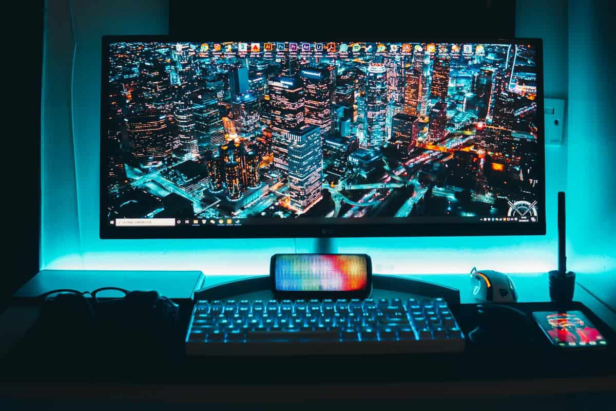1080p vs. 4K ultrawide monitor displaying cityscape with backlit keyboard, phone, and cyan ambient lighting