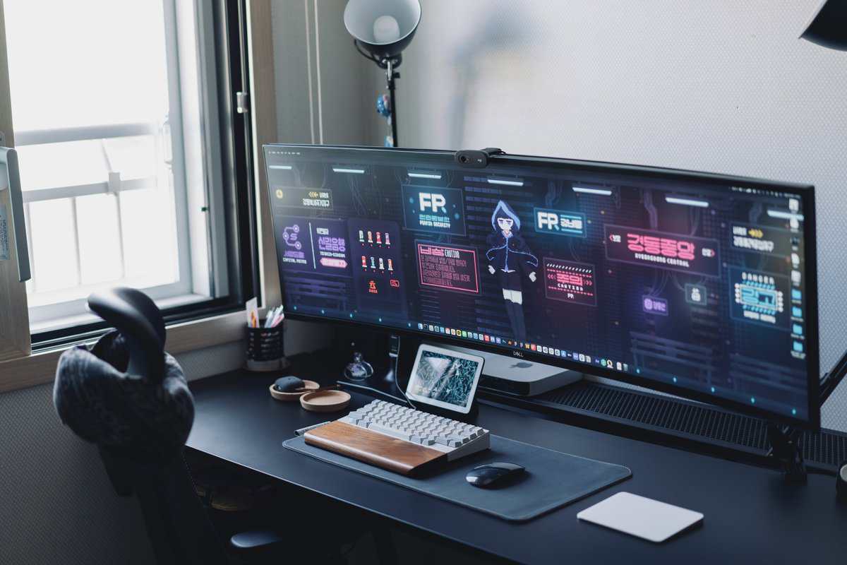 Gaming desk setup with super ultrawide curved monitor, white mechanical keyboard on wood wrist rest, tablet, and webcam for streaming on a black desk surface