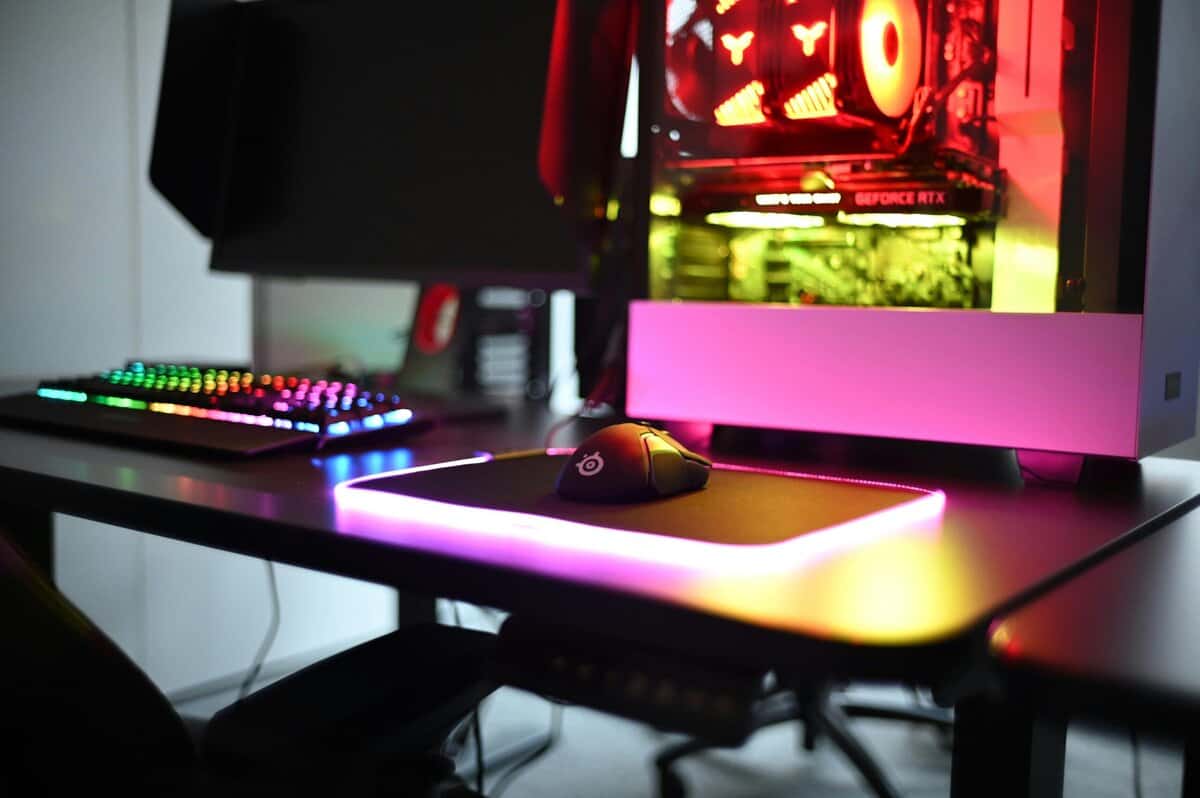 RGB gaming mouse pad with LED edge lighting on a gaming desk setup with SteelSeries mouse, RGB keyboard, and gaming PC