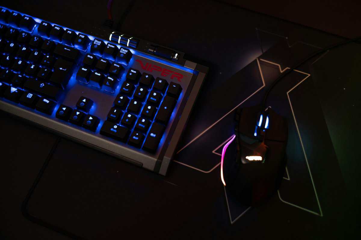 RGB gaming mouse on a black gaming mouse pad with geometric design next to a Patriot Viper mechanical keyboard with blue backlighting