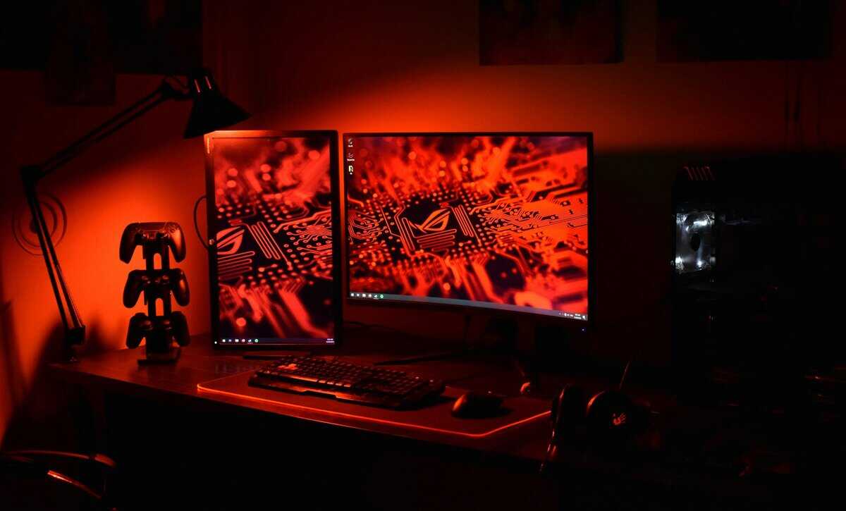 Dual 144Hz monitor ASUS ROG gaming setup with controller stand, mechanical keyboard, gaming headset, and PC with orange ambient lighting