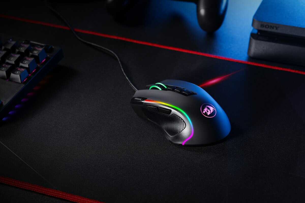 RGB gaming mouse on a black gaming mouse pad with red stitched edges, mechanical keyboard and PlayStation in the background