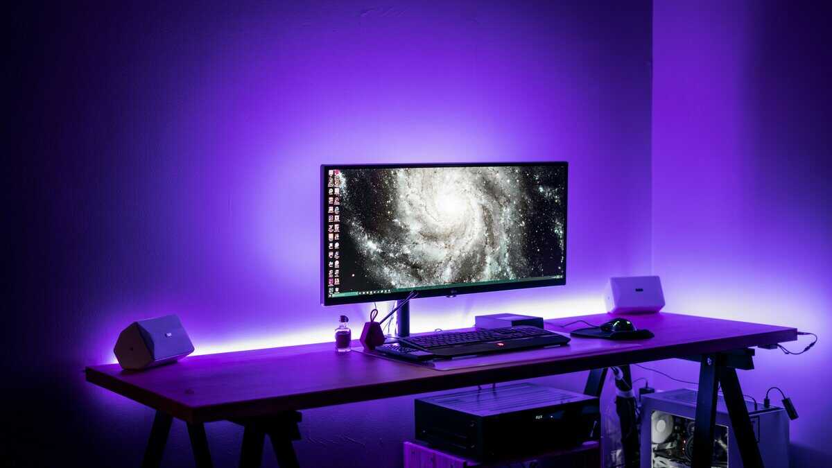 21:9 vs 16:9 ultrawide monitor with galaxy wallpaper and purple ambient lighting on minimalist desk setup