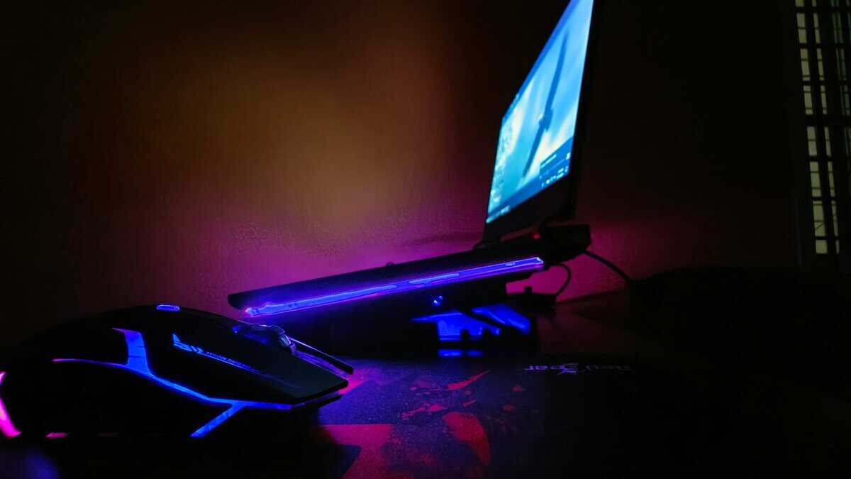 Gaming laptop under $600 on a cooling stand with blue LED lighting, gaming mouse, and mousepad in a dark room