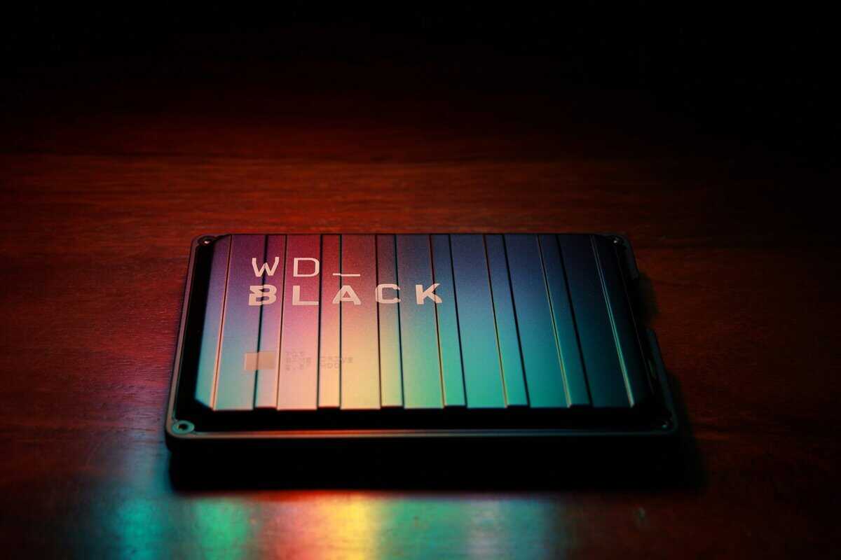 WD_BLACK P10 Game Drive on a wooden desk with colorful RGB light reflecting off its ridged metal surface, an affordable Xbox Series X storage expansion choice