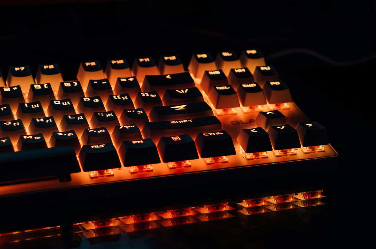 Close-up of a TKL keyboard with orange RGB backlighting illuminating black keycaps and arrow key cluster on a reflective dark surface