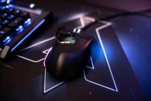 Wired RGB gaming mouse on a dark mousepad next to a blue keyboard, the wired side of the wired vs wireless gaming mouse debate