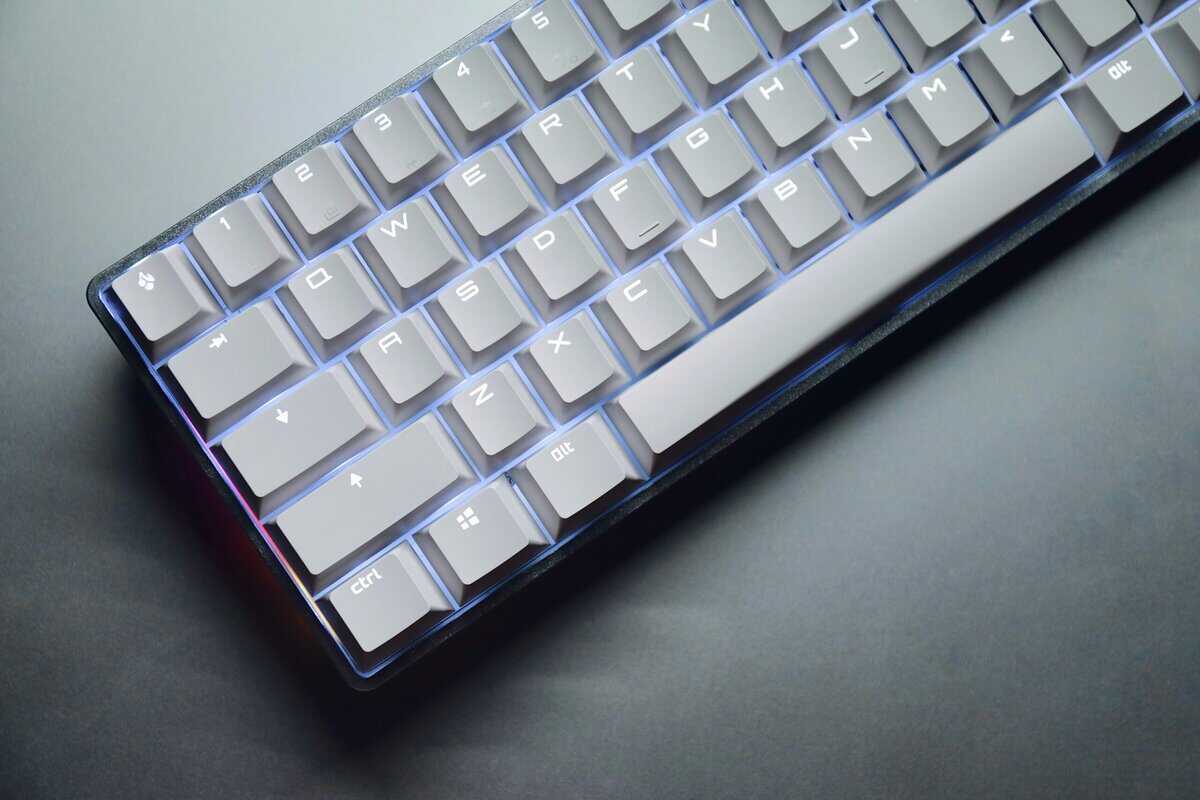 Compact 65% keyboard with white keycaps and blue RGB backlighting on a dark desk