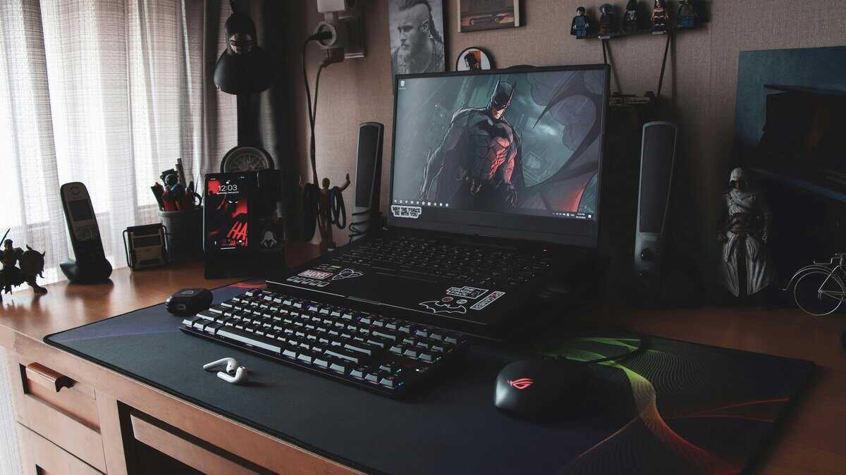 Gaming laptop under $600 displaying a game on a desk setup with gaming mouse, speakers, and collectible figures