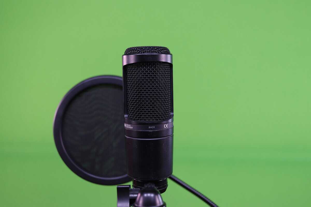 Black condenser microphone with a dual-layer microphone pop filter in a streaming setup with green screen background