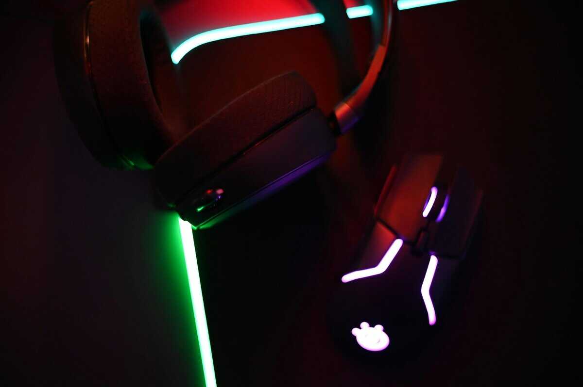 Close-up of a gaming headset with cyan LED lighting next to an RGB mouse under red ambient glow, showcasing the peripherals that pair with the best noise cancelling headset