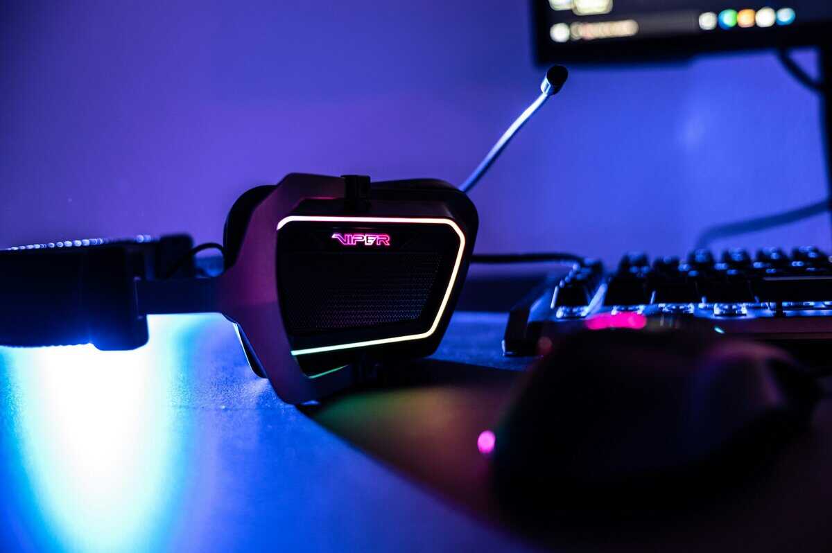 RGB gaming headset with boom mic next to a keyboard and mouse under blue ambient lighting, showcasing the best cheap over ear headphones setup