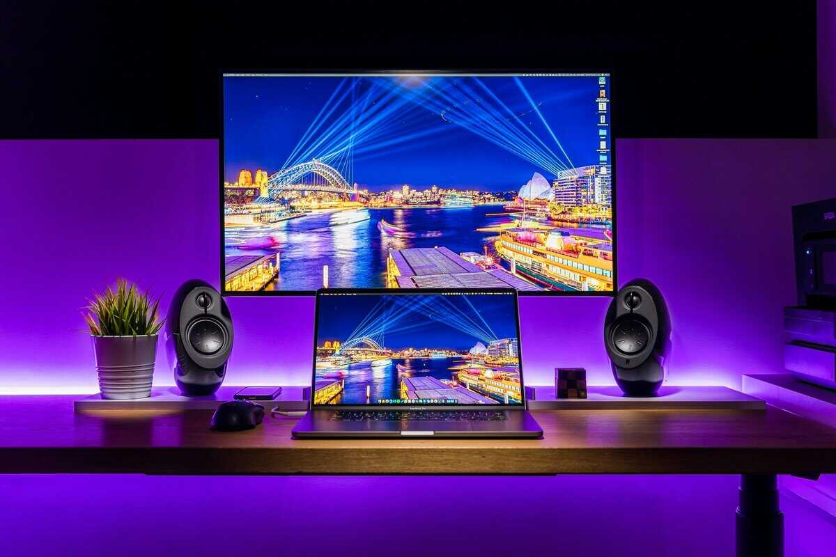 Gaming laptop connected to an external monitor with purple backlighting and speakers, showing how a laptop fits into a gaming laptop vs desktop setup