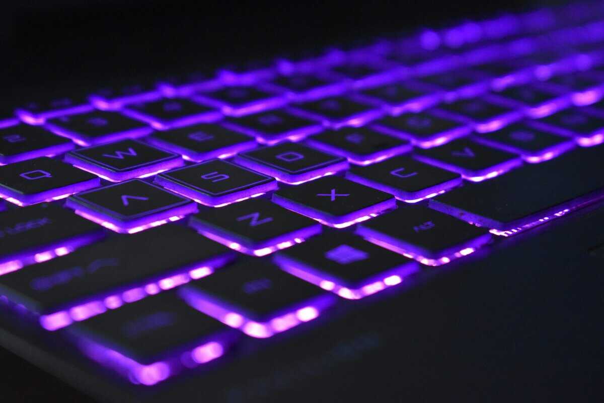 Close-up of a gaming laptop keyboard with vibrant purple RGB backlighting between the keys, showcasing the build quality buyers should expect from an RTX 5090 laptop