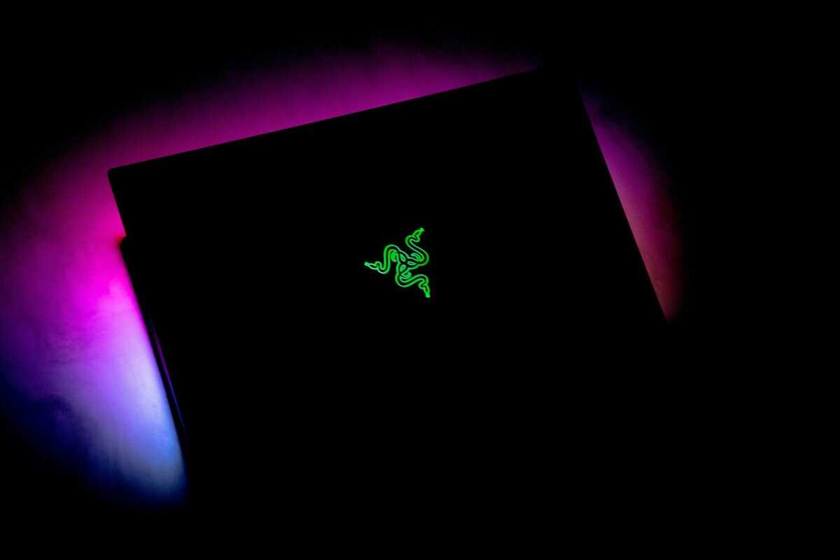 Closed Razer gaming laptop lid with glowing green triple-snake logo surrounded by purple and pink ambient lighting, representing the premium RTX 5090 laptop tier