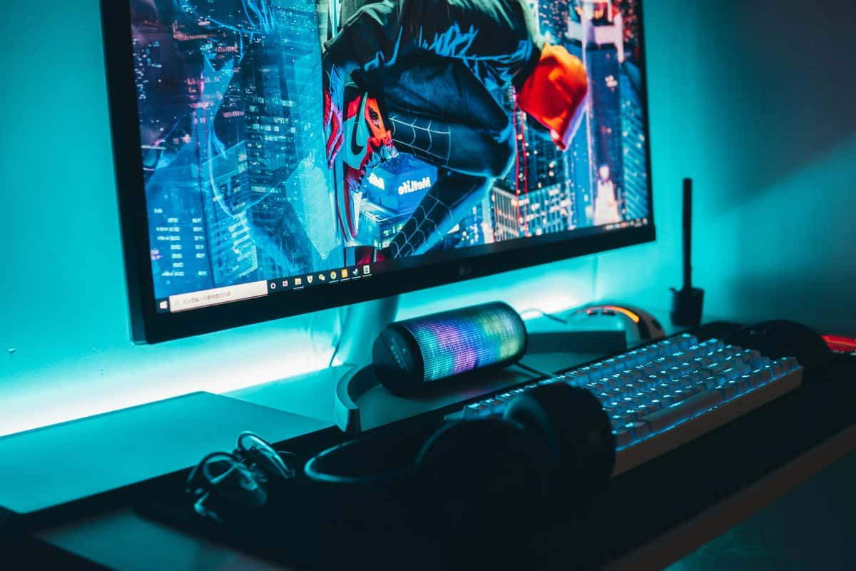 Gaming monitor displaying Spider-Verse art with an RGB keyboard and teal ambient lighting, a budget-friendly setup in the 1440p vs 4K gaming debate