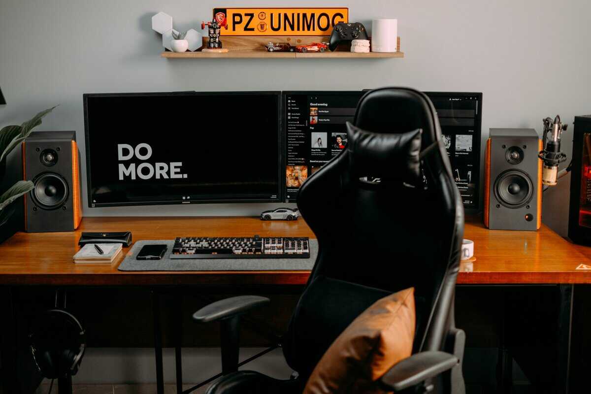 Black gaming chair with an orange pillow accent at a dual monitor desk, an example of how the best budget gaming chair fits into a clean setup