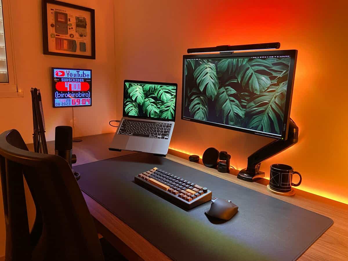 Widescreen monitor floating on a gas-spring arm in a warm gaming setup, showing why picking the best monitor arm matters for ultrawide builds