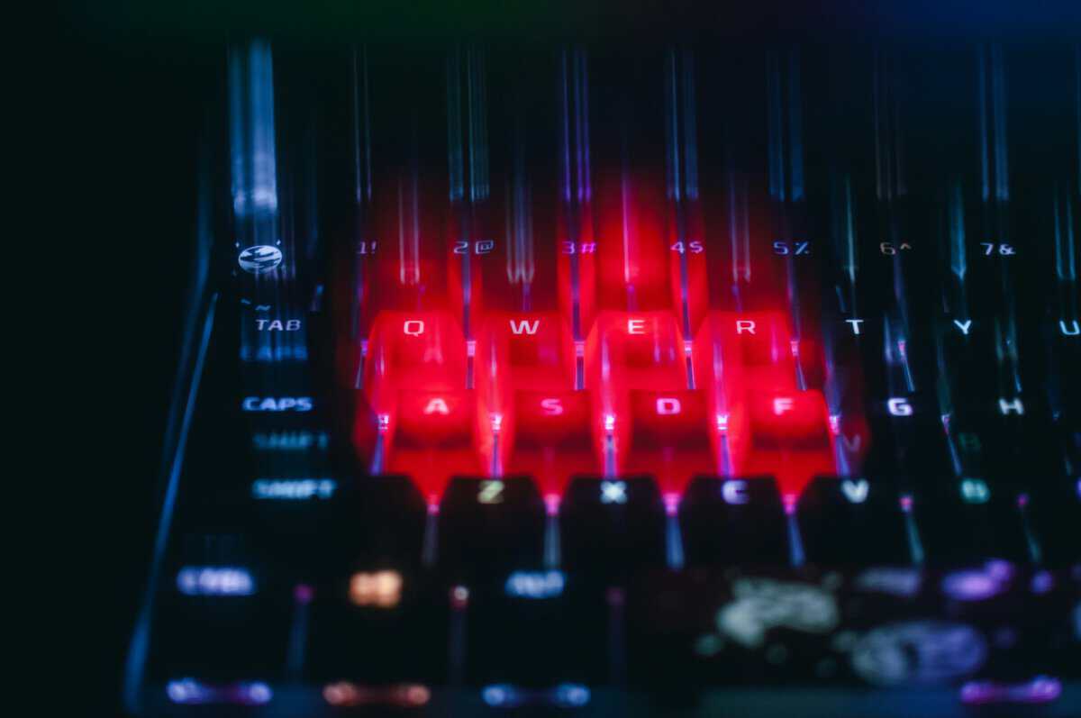 Close-up of a red-backlit mechanical keyboard showing dust and crumbs collected around the WASD and spacebar area, the kind of buildup the how to clean a mechanical keyboard process targets