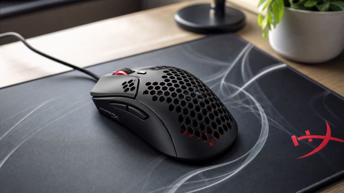 Black honeycomb-shell HyperX wired gaming mouse on a branded mouse pad with a desk plant behind it, a lightweight pick for the best mouse for Tarkov