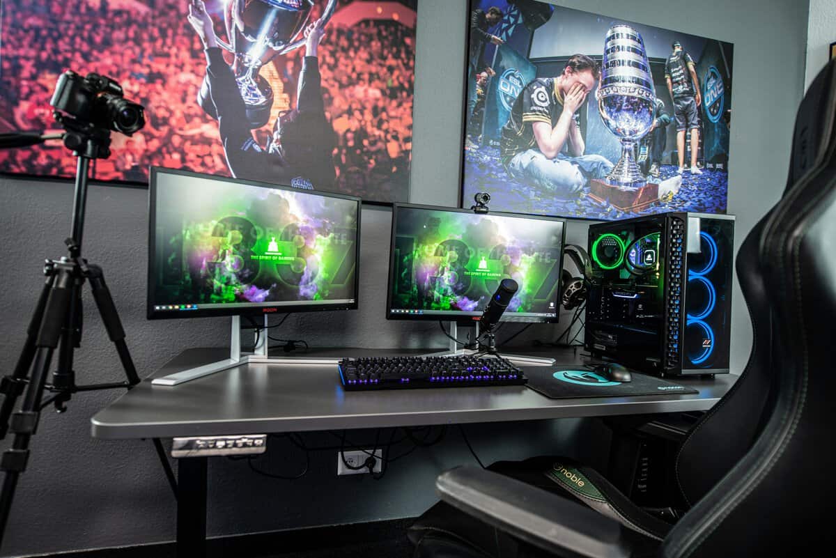 A dark RGB-lit dual-monitor battlestation with a tripod-mounted camera and gaming chair, showing the best standing desk for gaming in a streaming setup