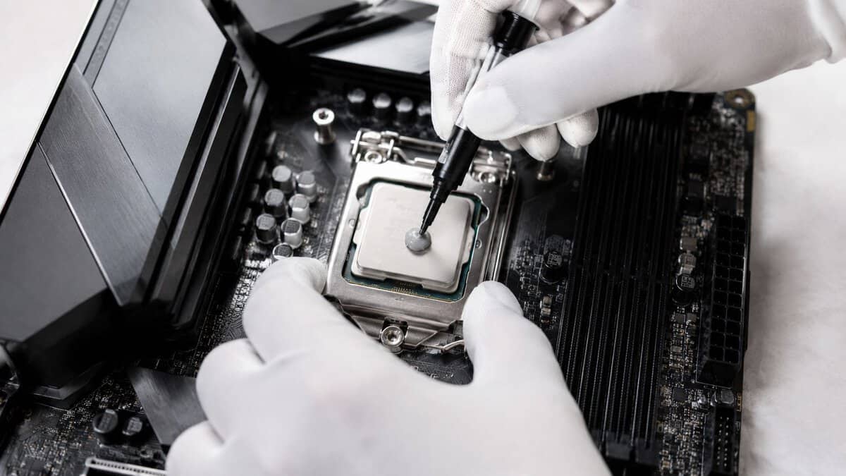 Gloved hands applying the best thermal paste as a centered dot on a CPU before mounting the cooler