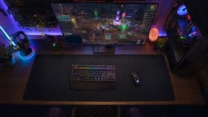 Top-down view of an RGB battlestation with a raid on screen and keyboard and mouse sharing one desk-scale pad, the setup the best MMO mousepad anchors