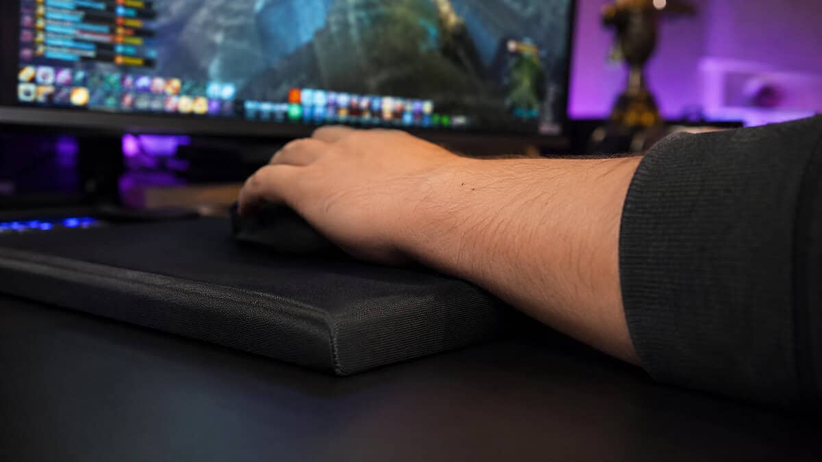 Wrist resting on the edge of a thick cushioned cloth pad with hotbars glowing behind, the comfort a best MMO mousepad is built around