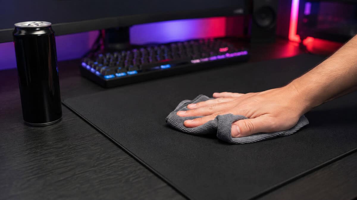 Hand wiping a black cloth pad with a microfiber cloth beside an energy drink can, the care routine that keeps the best MMO mousepad alive