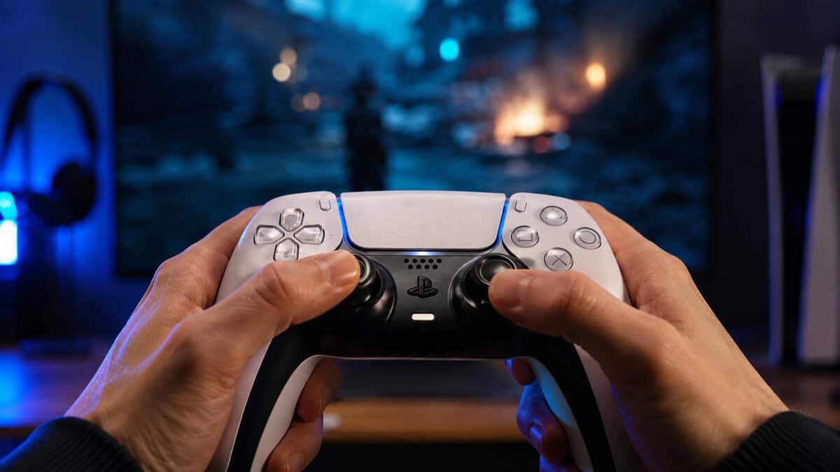 Two hands gripping a white DualSense with a game glowing on the screen behind it, the default answer in any best PS5 controller conversation