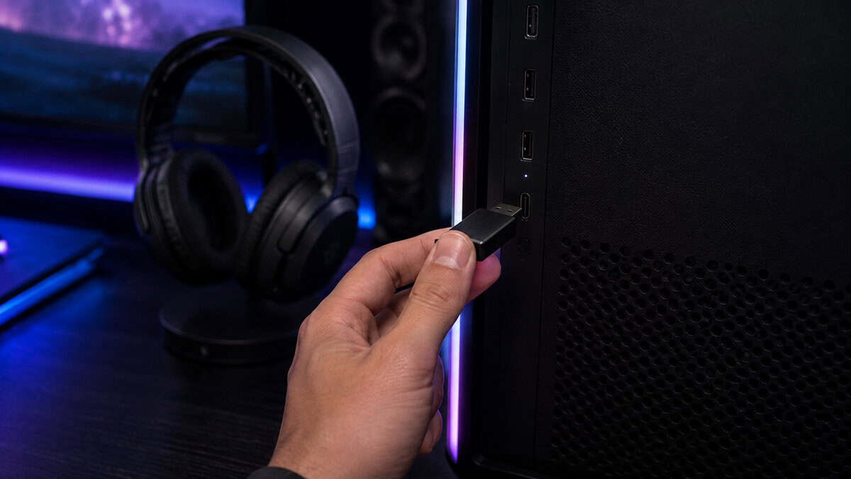 A hand plugging a small USB wireless dongle into a PC front port, the connection that makes the best wireless gaming headset feel wired