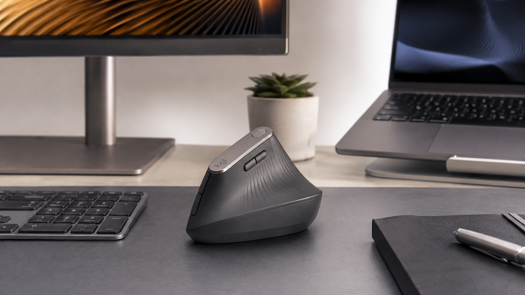 Graphite Logitech vertical mouse beside a full-size keyboard, monitor and laptop on a bright office desk, the sculpted shell to look for in the best vertical mouse