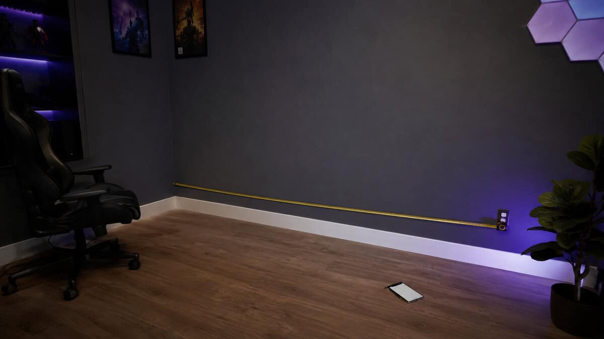 Tape measure stretched along the wall of an empty game room corner before an l-shaped gaming desk purchase