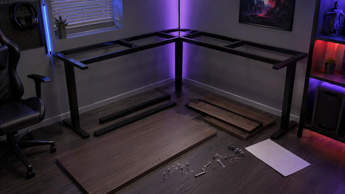 Flat-pack frame and panels of an l-shaped gaming desk mid-assembly in the corner of an RGB game room