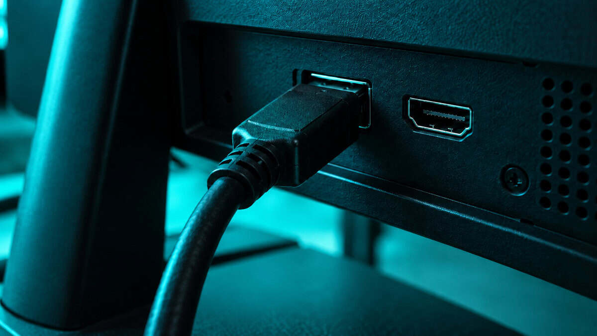 Close-up of a monitor rear panel with a DisplayPort cable plugged in beside an HDMI port under teal light, the inputs that matter on the best monitor for Fortnite