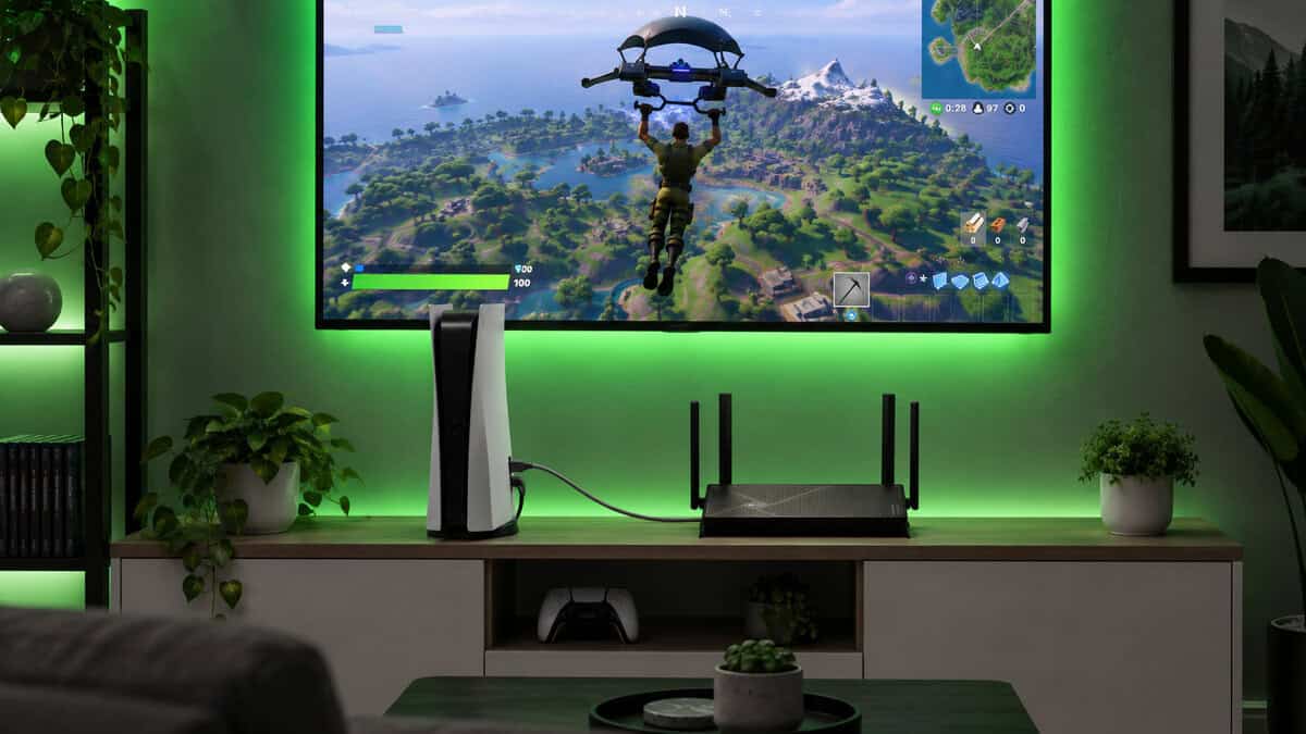 PS5 console cabled to a four-antenna wifi 7 router on a TV stand under a green-lit TV showing Fortnite