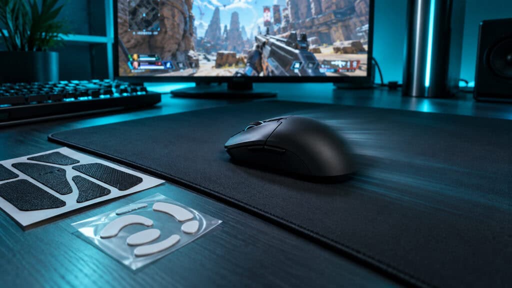 Lightweight black wireless mouse sliding across a speed pad in teal light beside spare grip tape and mouse skates, with an Apex Legends firefight on screen, a light pick for the best wireless gaming mouse