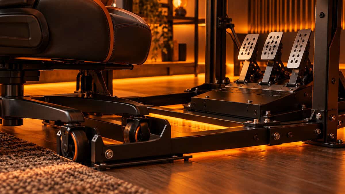 Close view of a gaming chair's casters locked into a metal cradle beside a three-pedal plate under amber light, the chair fix that makes a stand feel like a sim racing cockpit