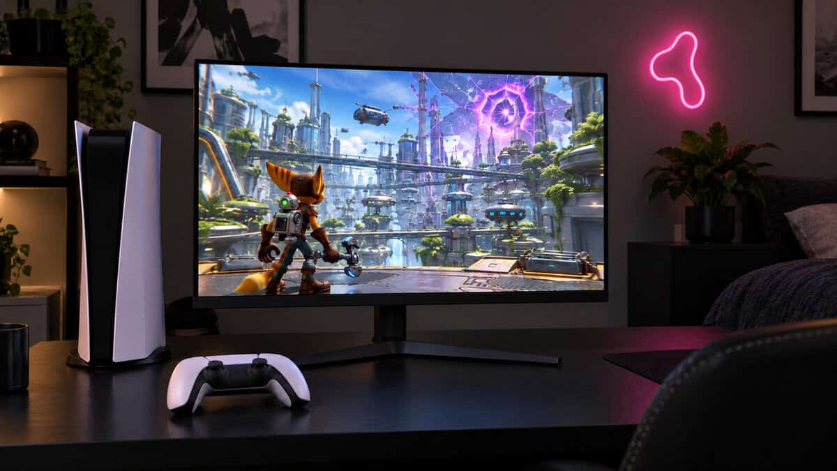 White tower game console and controller beside a 27-inch monitor showing a colorful sci-fi platformer, a magenta neon sign on the wall, a console desk where 1080p vs 1440p output matters