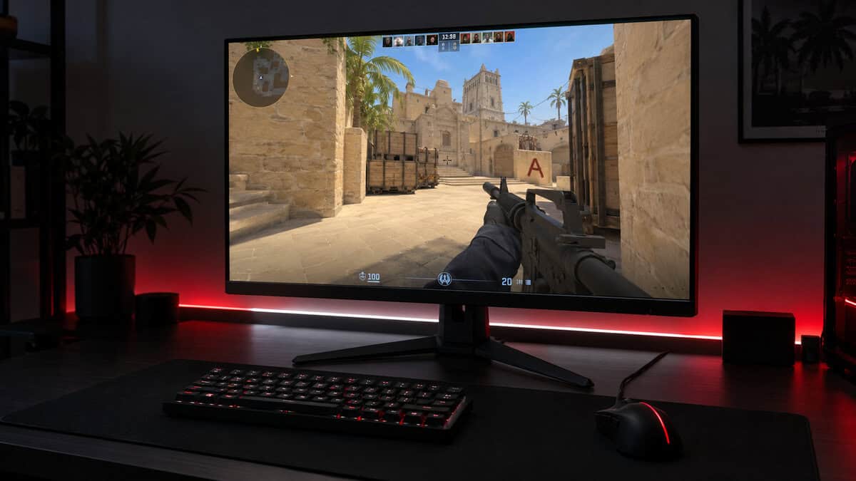 27-inch flat gaming monitor on a dark desk showing a Counter-Strike 2 round on Mirage near the A site, a red and white light strip glowing behind it, with a compact backlit keyboard and wired mouse in front of the best 360Hz monitor