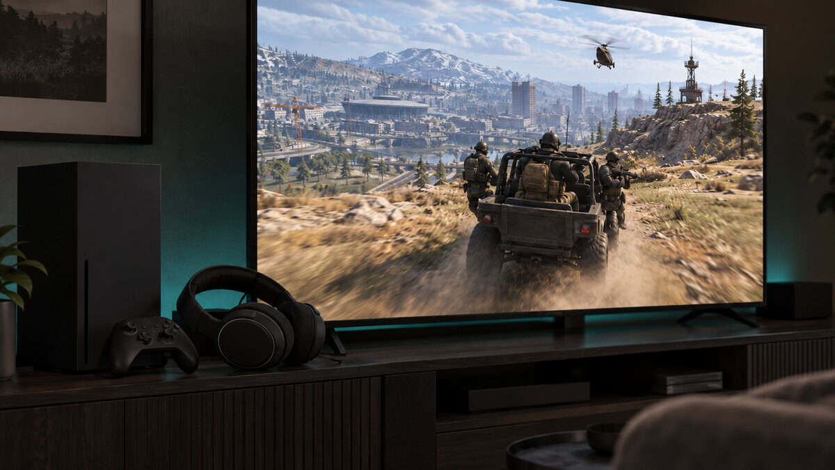 Black tower console, controller and wireless headset on a TV stand while a squad rides an off-road vehicle across a Warzone hillside on screen, cyan-teal light glowing behind the TV, a living room console setup built around the best headset for Warzone