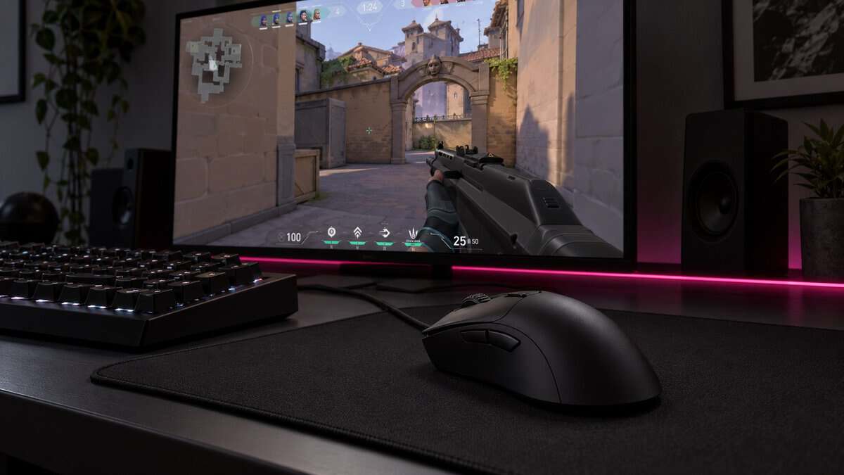 Black right-handed ergonomic wired mouse with a long sloped back on a black cloth pad beside a keyboard, an example of the best mouse for claw grip, with Valorant on the monitor