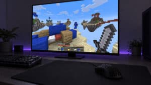 Black lightweight honeycomb gaming mouse on a large cloth pad in front of a monitor showing a Minecraft Bedwars fight on sky islands, a violet light strip glowing behind the screen, a PvP desk built around the best mouse for Minecraft