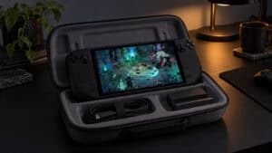 Steam Deck playing Hades II inside an open grey zip carrying case with a coiled USB-C charger and a small dock, the kind of storage the best Steam Deck case offers, on a dark desk lit by an amber lamp