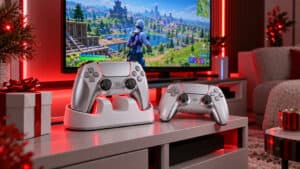 Gifts for gamers on a TV stand: a silver PS5-style controller in a white twin charging dock, a second controller and a wrapped present, with a battle royale game on the TV under red lighting