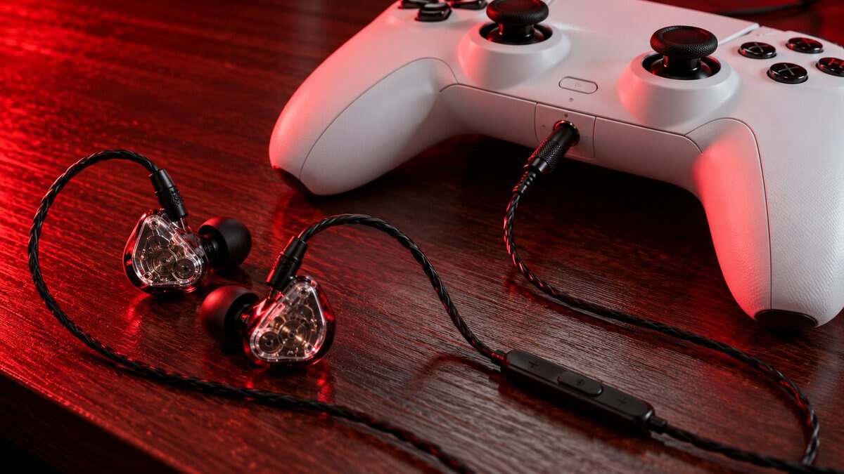 Clear-shell iems for gaming with an inline mic remote, plugged into the headphone jack of a white controller on a red-lit wood desk