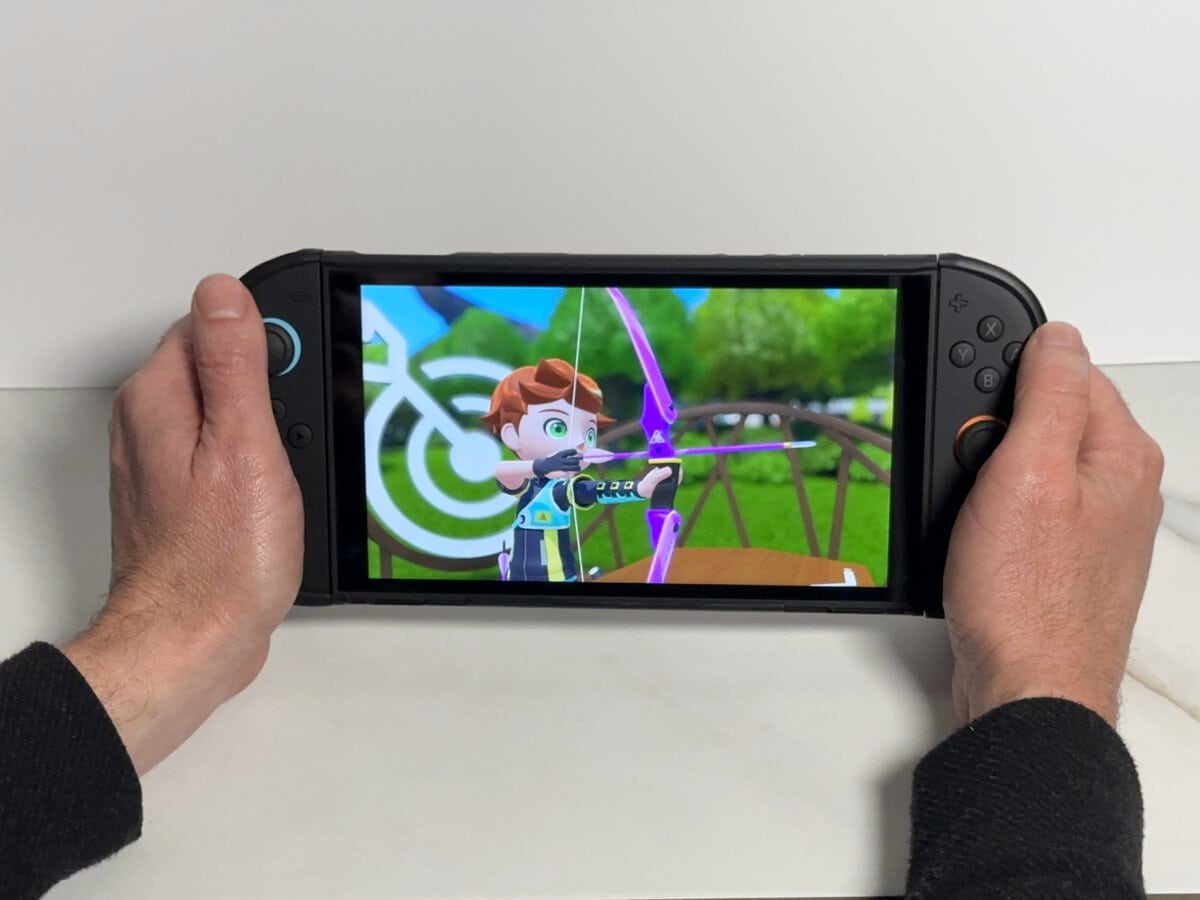 Two hands holding a Switch 2 in the JSAUX GoJoy case by its grips with an archery game on screen